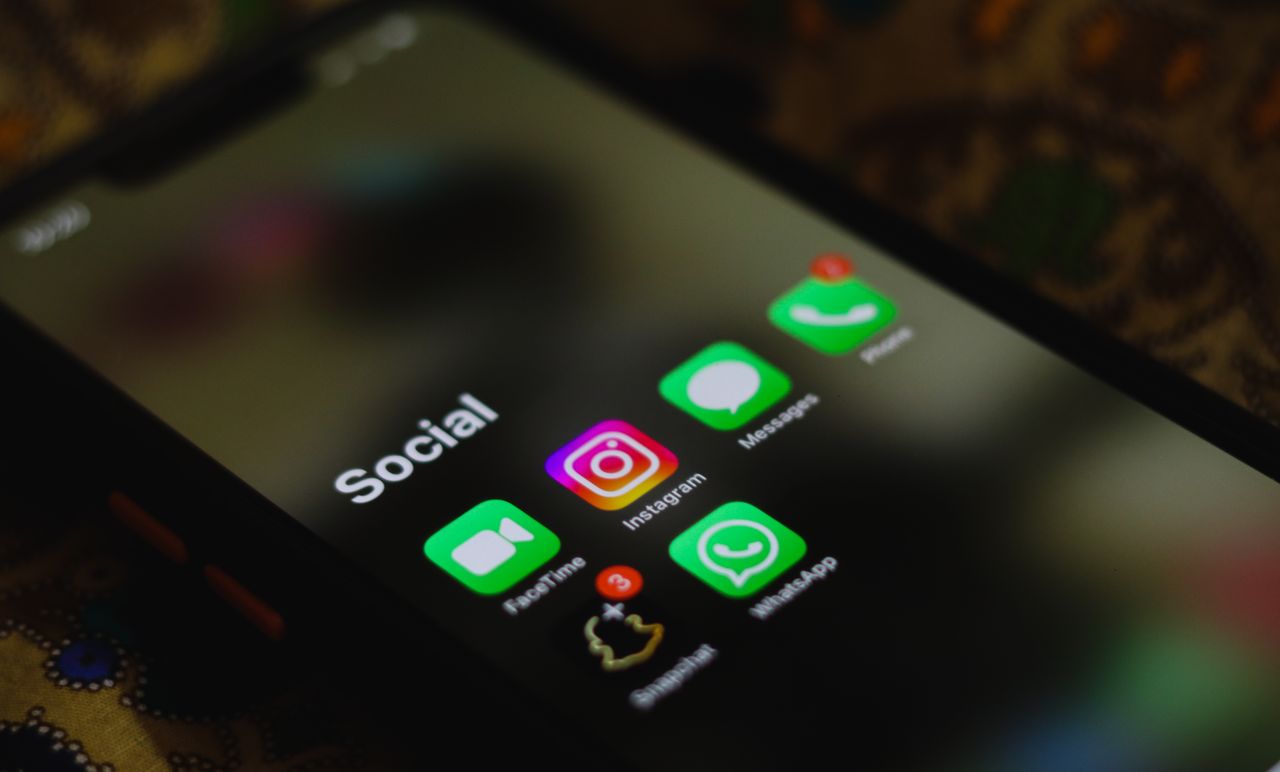 Phone screen showing a 'Social' folder with apps (Facebook, Instagram, Messages, WhatsApp) on a blurred background.