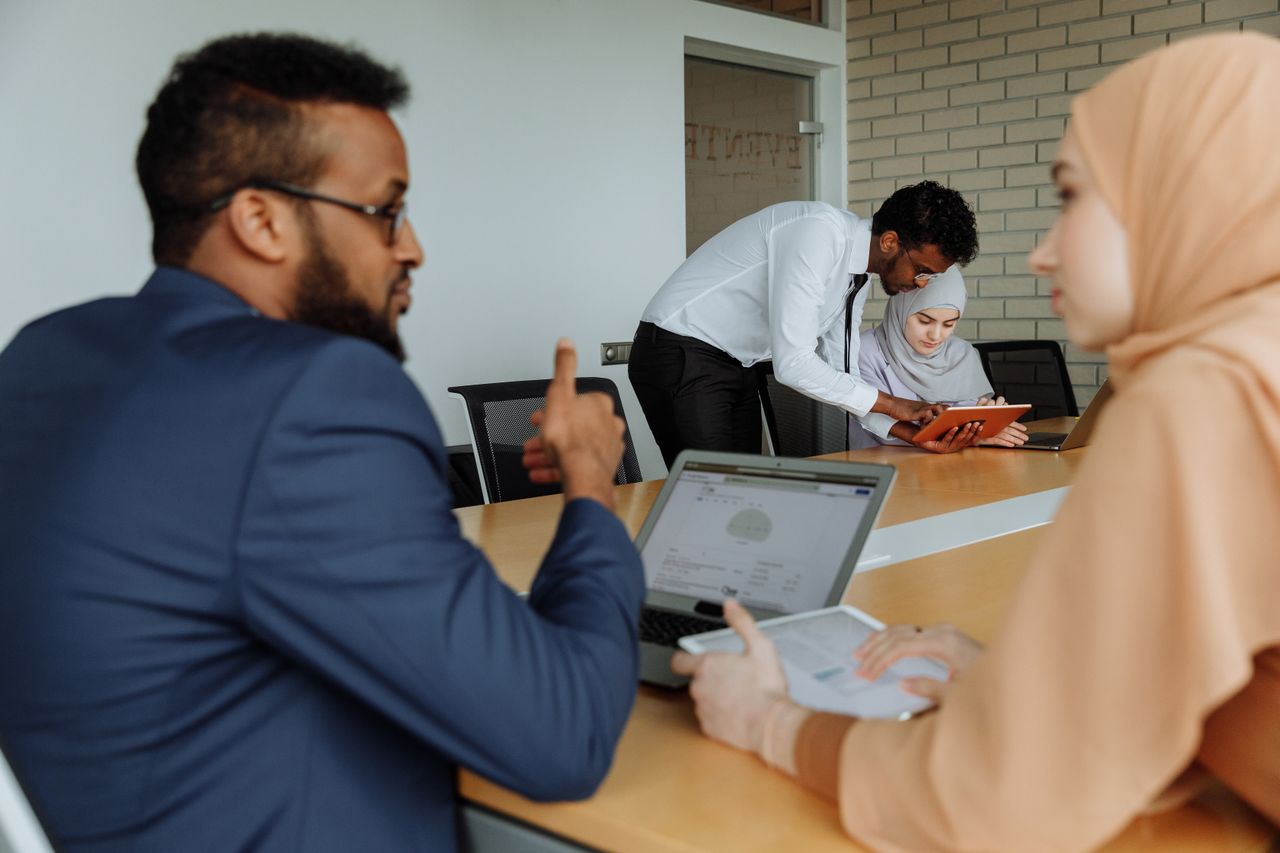 pexels-thirdman-7993567 - Blog Muslim Marriage Services Diverse coworkers collaborate at a conference table; a man leans over to help a woman with a tablet.